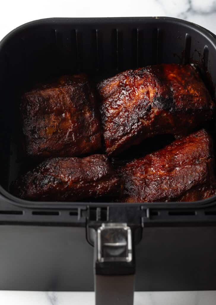 Baby back ribs in an air fryer, coated in bbq sauce.