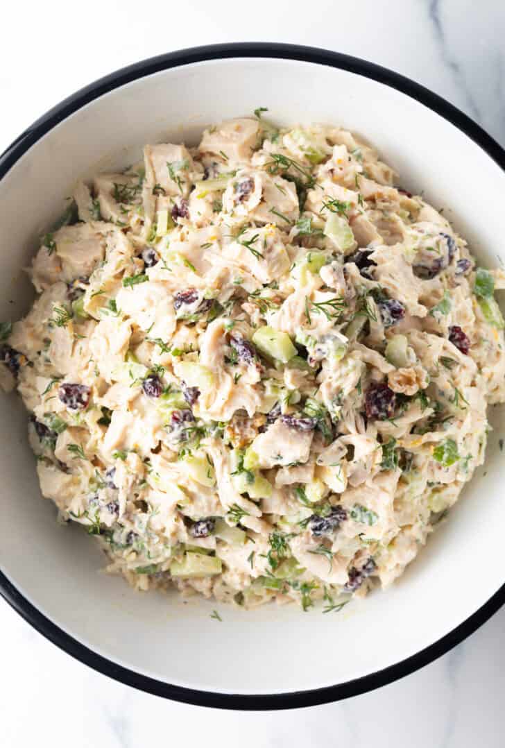 White bowl of chicken salad with walnuts and cranberries.