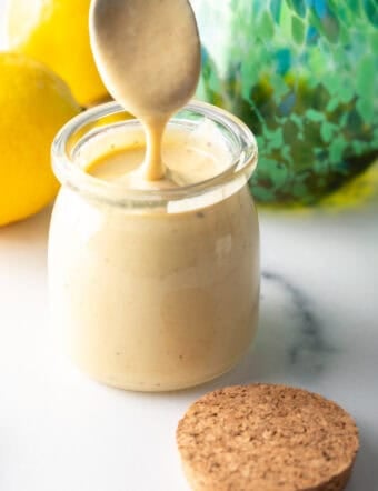 Spoon of dressing being held above a jar of tahini dressing.