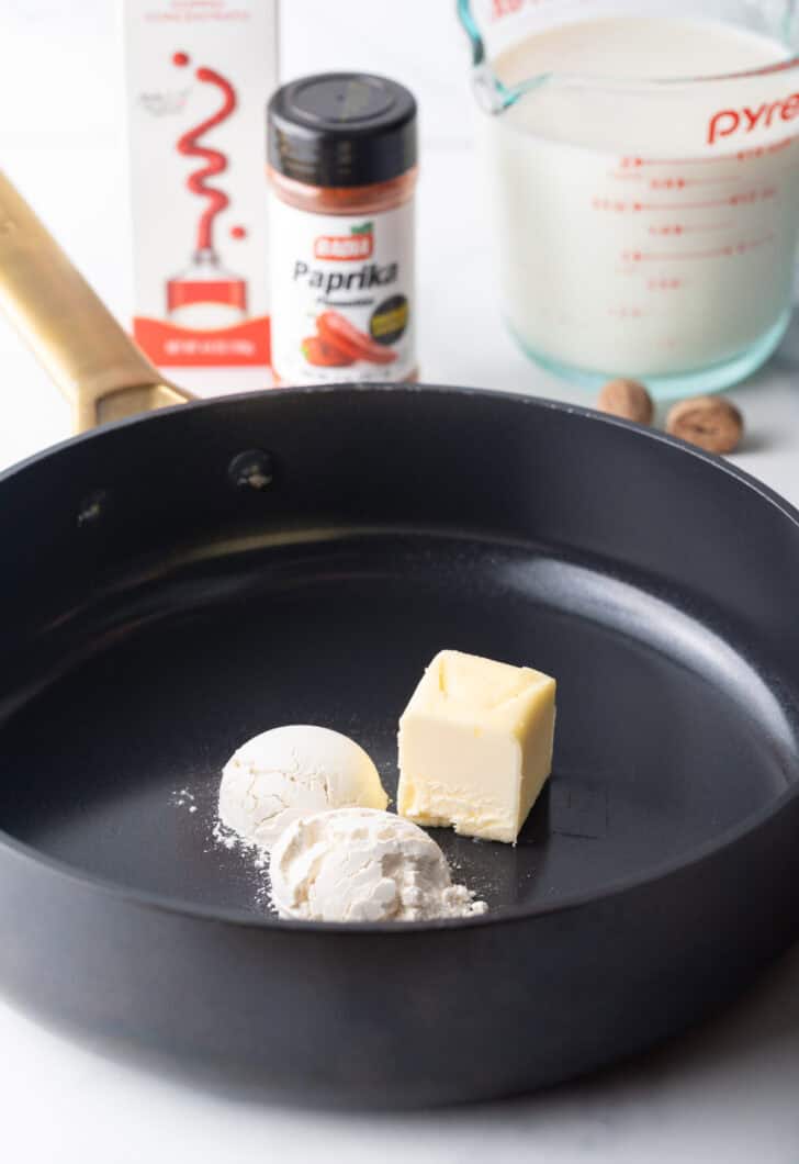 A black skillet with two small scoops of flour and a large cube of flour.