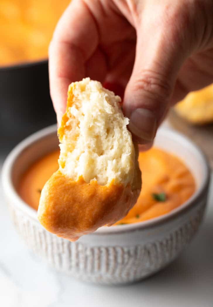 Hand holding a biscuit dipped in gravy to camera.