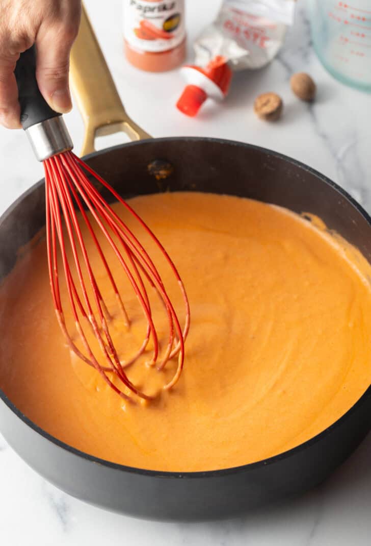 Deep black skillet with red gravy and a red whisk.