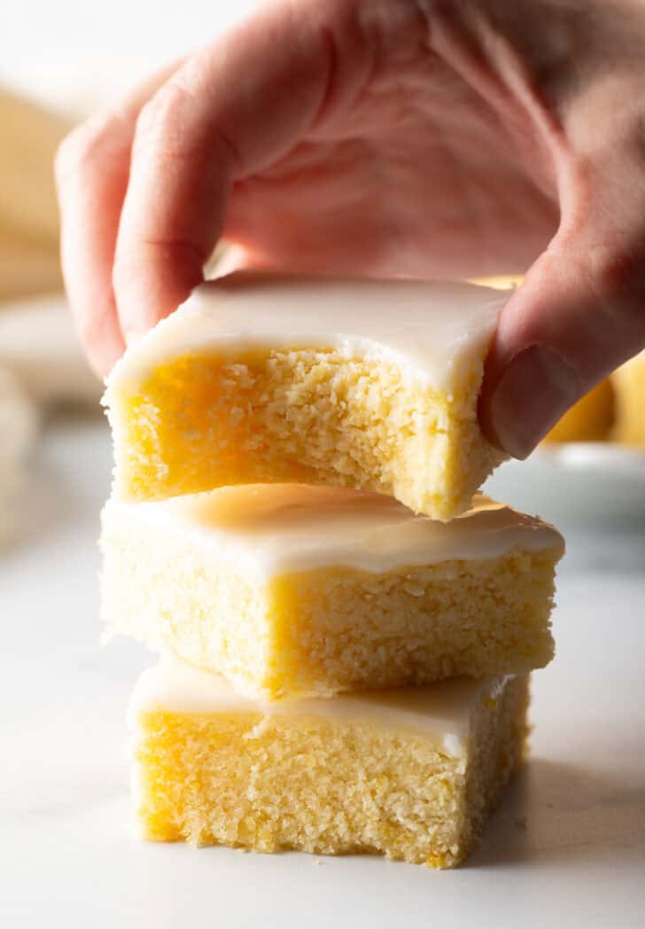 Stack of 2 brownies with a third brownie being held to camera. A bit has been taken from the lemon blondie bar.