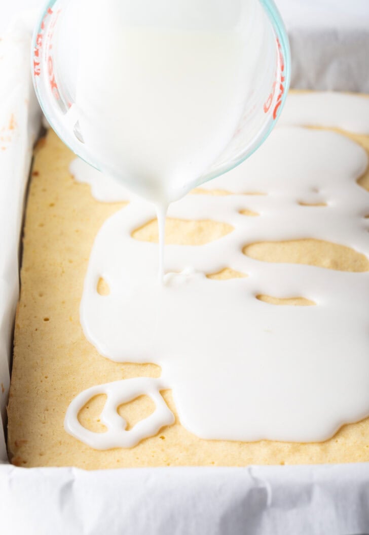 Pouring the top white lemon glaze over the baked blondies in a large baking pan.