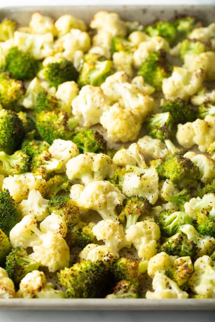 Cauliflower and broccoli florets spread across a baking sheet.
