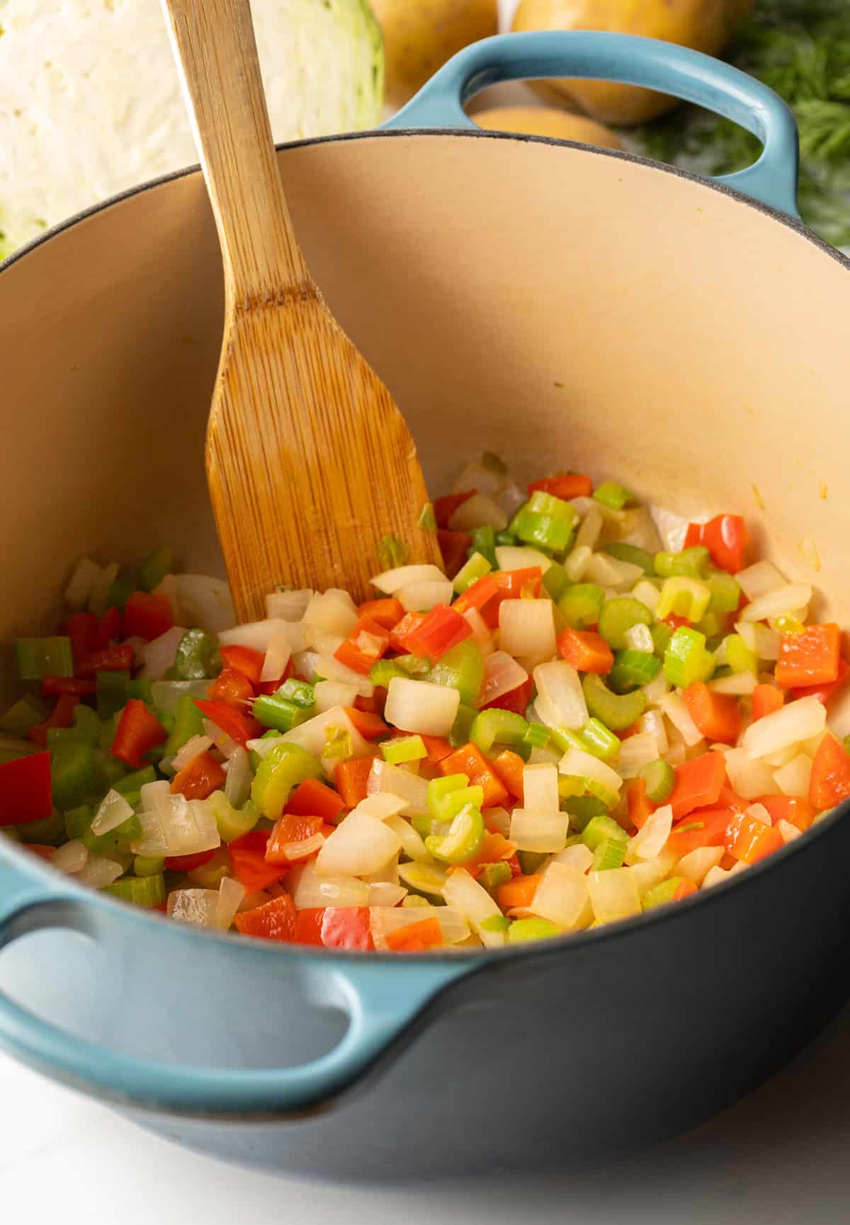 Cooking iced onion, carrots, bell pepper and celery in a large blue cooking pot.