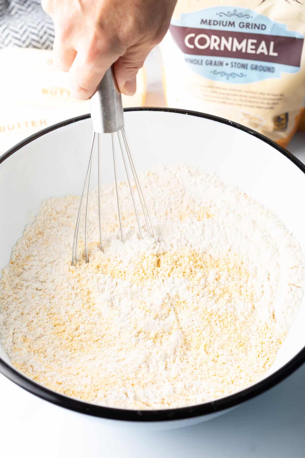 Hand whisking a bowl filled with dry ingredients for cornbread. 