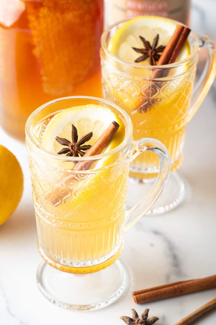 2 glass handled mugs with hot toddy, garnished with star anise and a cinnamon stick.