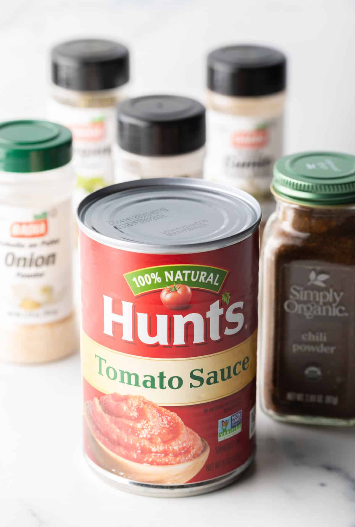 Ingredients you need: Can of tomato sauce, various spices in jars like chili powder, ground cumin, garlic powder, and onion powder.
