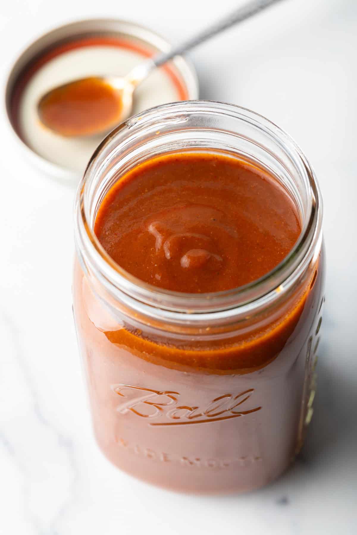 Top down view of red sauce in a large glass jar.