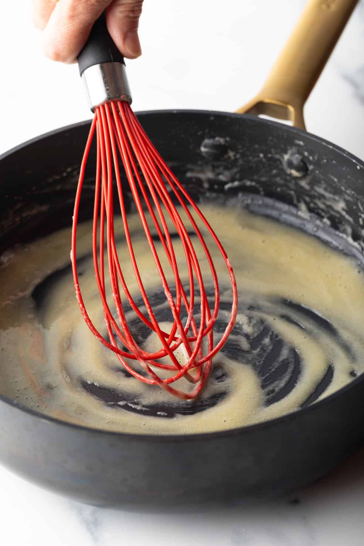 Red whisk stirring butter in a black skillet.