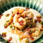Green bowl filled with cheesy grits and topped with Cajun shrimp and chopped bacon.