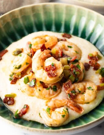 Green bowl filled with cheesy grits and topped with Cajun shrimp and chopped bacon.