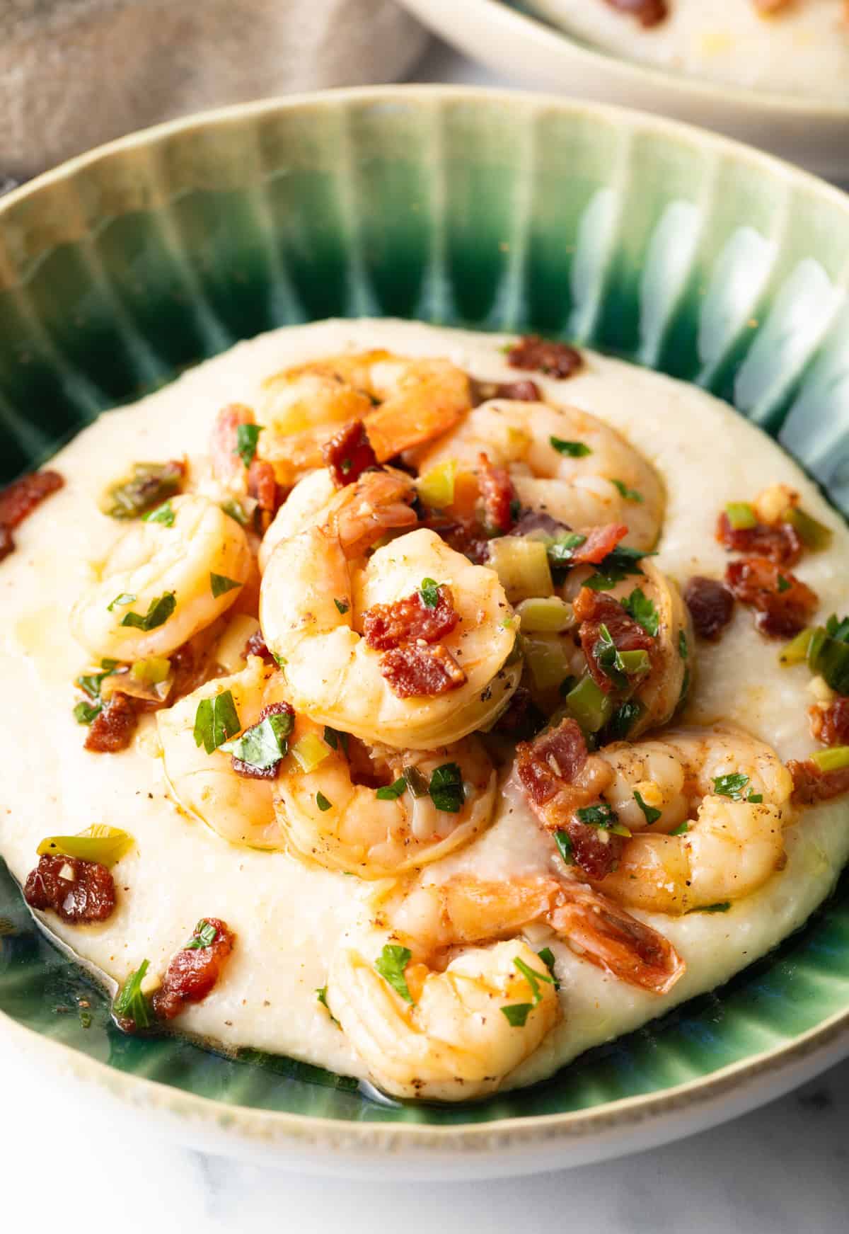 Green bowl filled with cheesy grits and topped with Cajun shrimp and chopped bacon.