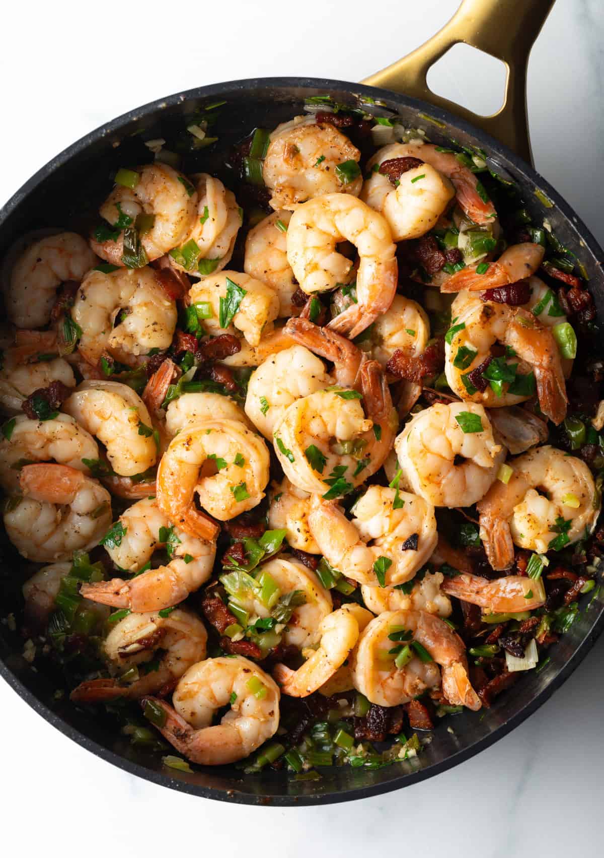 Top down cast iron skillet filled with cooked shrimp.