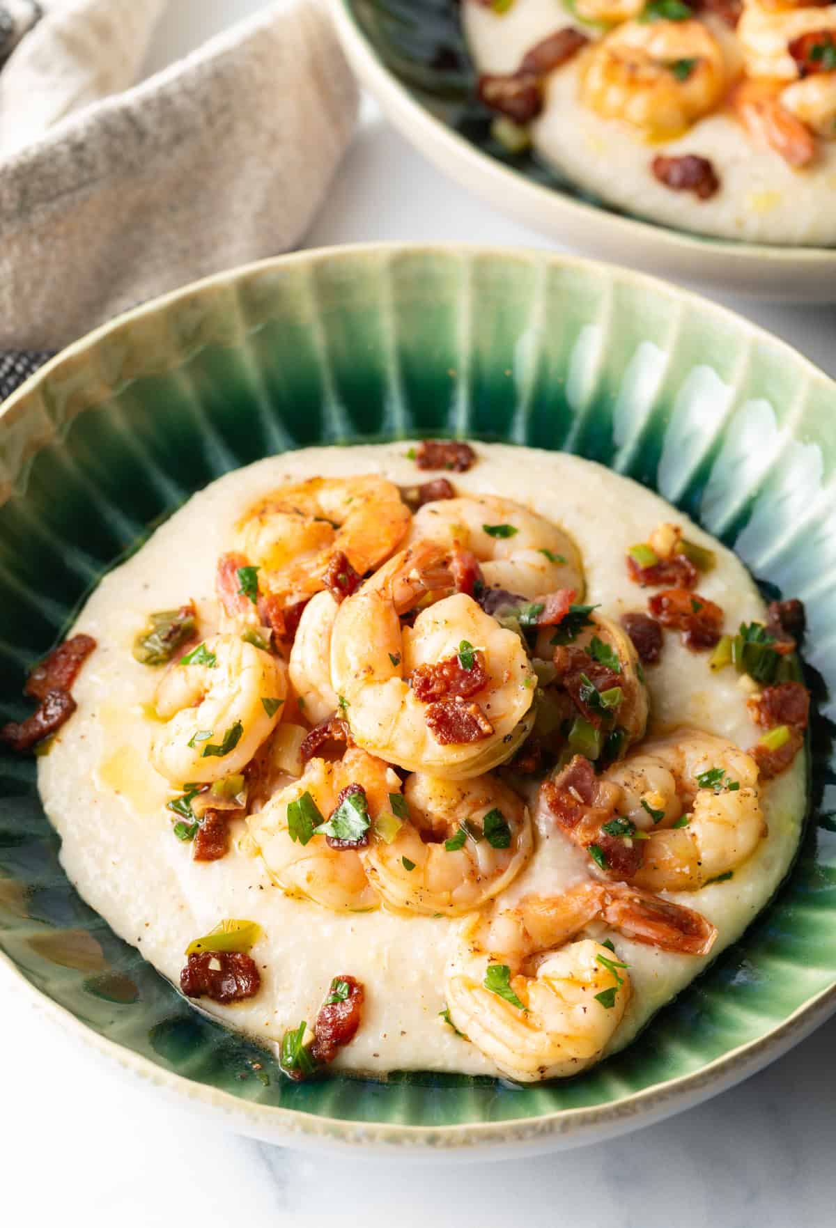 Green bowl filled with cheesy grits and topped with Cajun shrimp and chopped bacon.