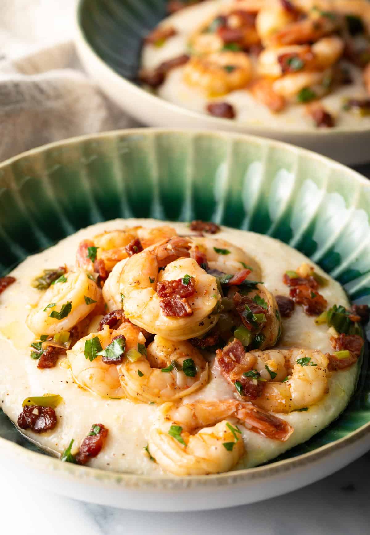 Green bowl filled with cheesy grits and topped with Cajun shrimp and chopped bacon.