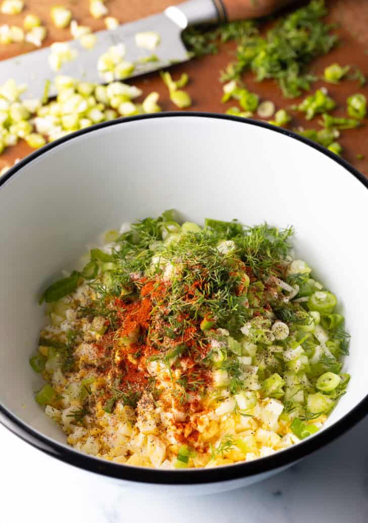 Chopped eggs, green onions, fresh herbs and paprika in a white bowl.