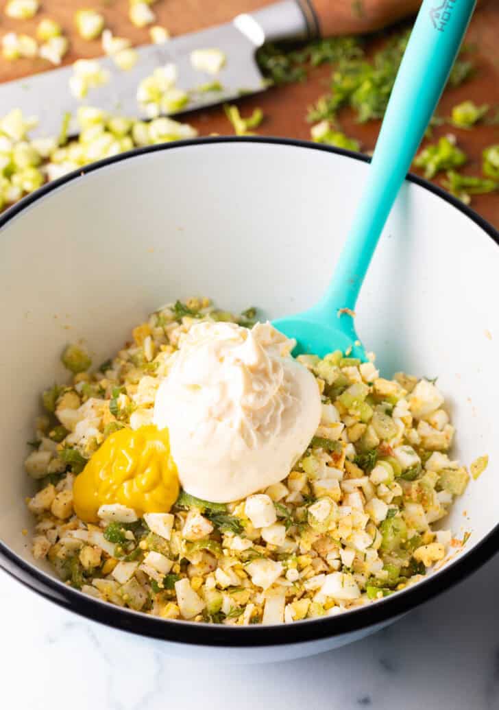 White bowl with scoops of chopped eggs, green onions, herbs and mayonnaise.