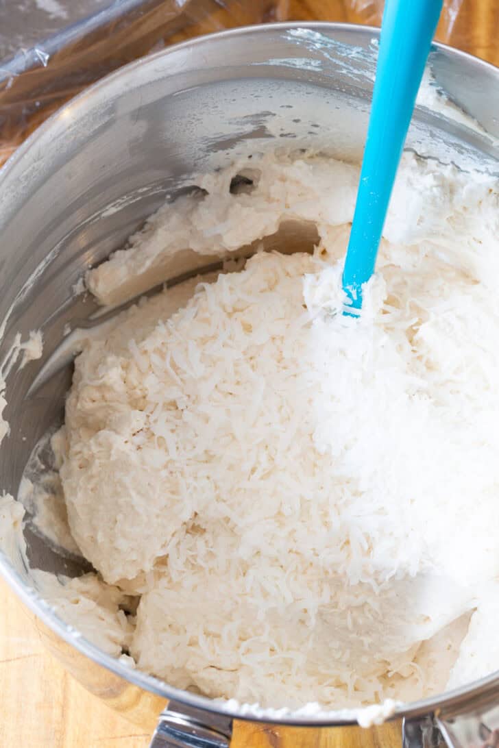 Stirring whipped cream in a metal bowl with a blue spatula.