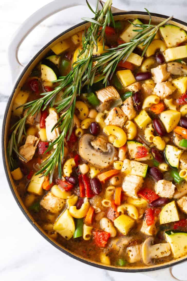 White pot brimming with chicken minestrone soup and springs of fresh rosemary.