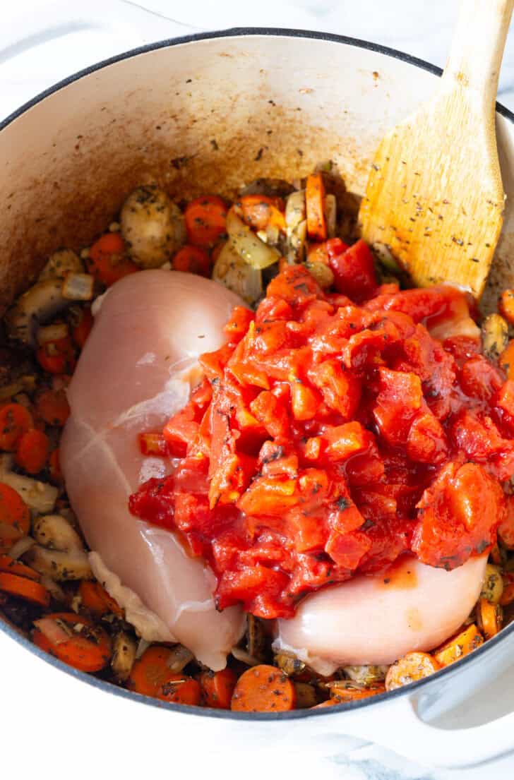 Two chicken breasts in a pot with tomatoes, zucchini, and carrots.