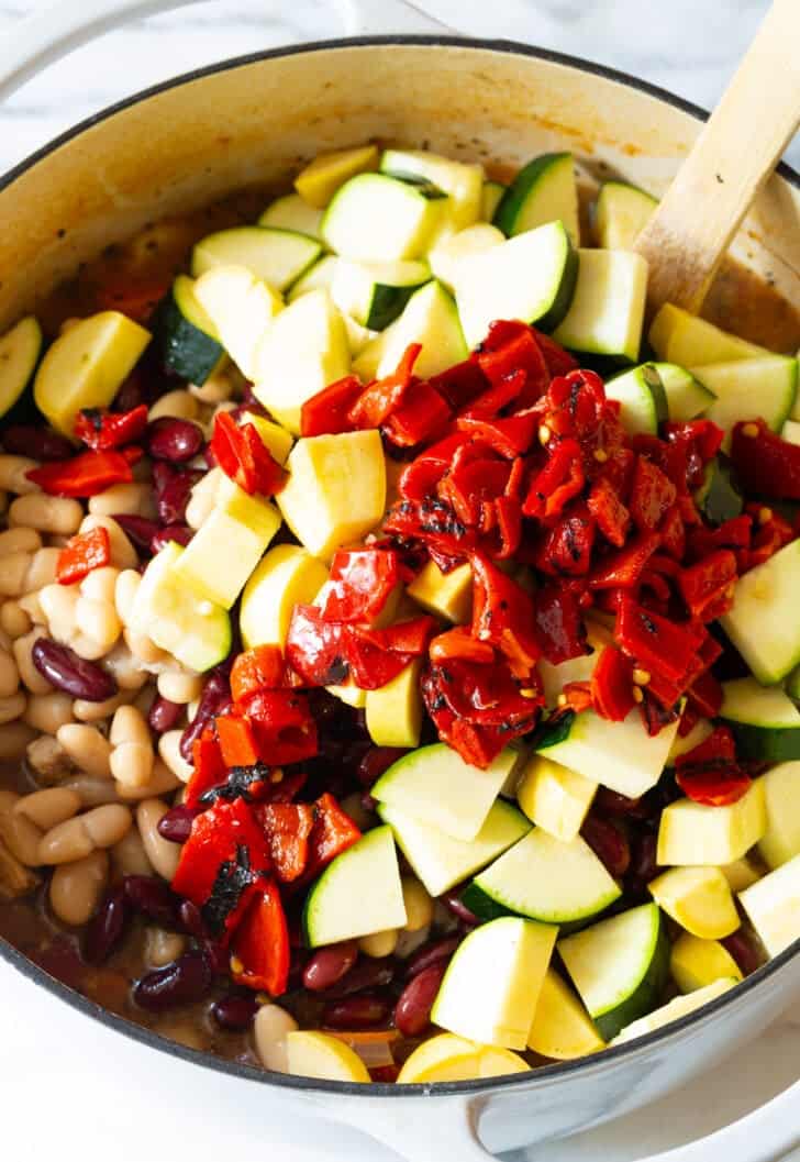 Adding chopped roasted red peppers to a pot with chopped zucchini and carrots.