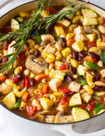 White pot brimming with chicken minestrone soup and springs of fresh rosemary.