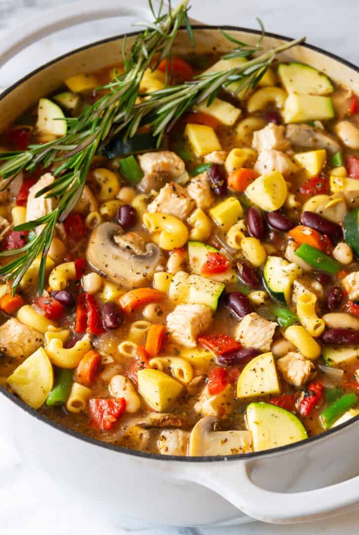 White pot brimming with chicken minestrone soup and springs of fresh rosemary.