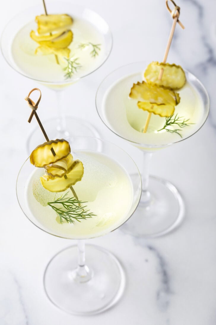 Three dirty martinis made with pickle juice and gin, garnished with skewers stacked with dill pickle slices.