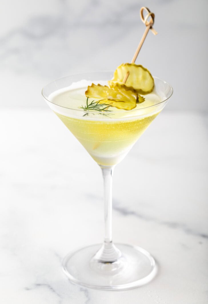 A martini glass with dill pickle juice and gin, garnished with pickle slices.