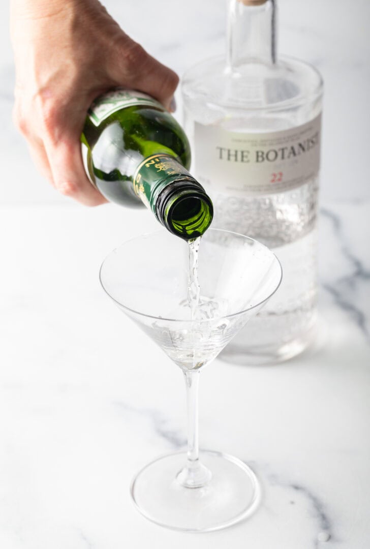 Hand pouring gin from a bottle into a martini glass.