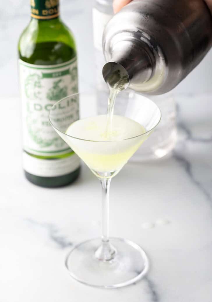 Pouring liquid from a metal cocktail shaker into a classic martini glass.