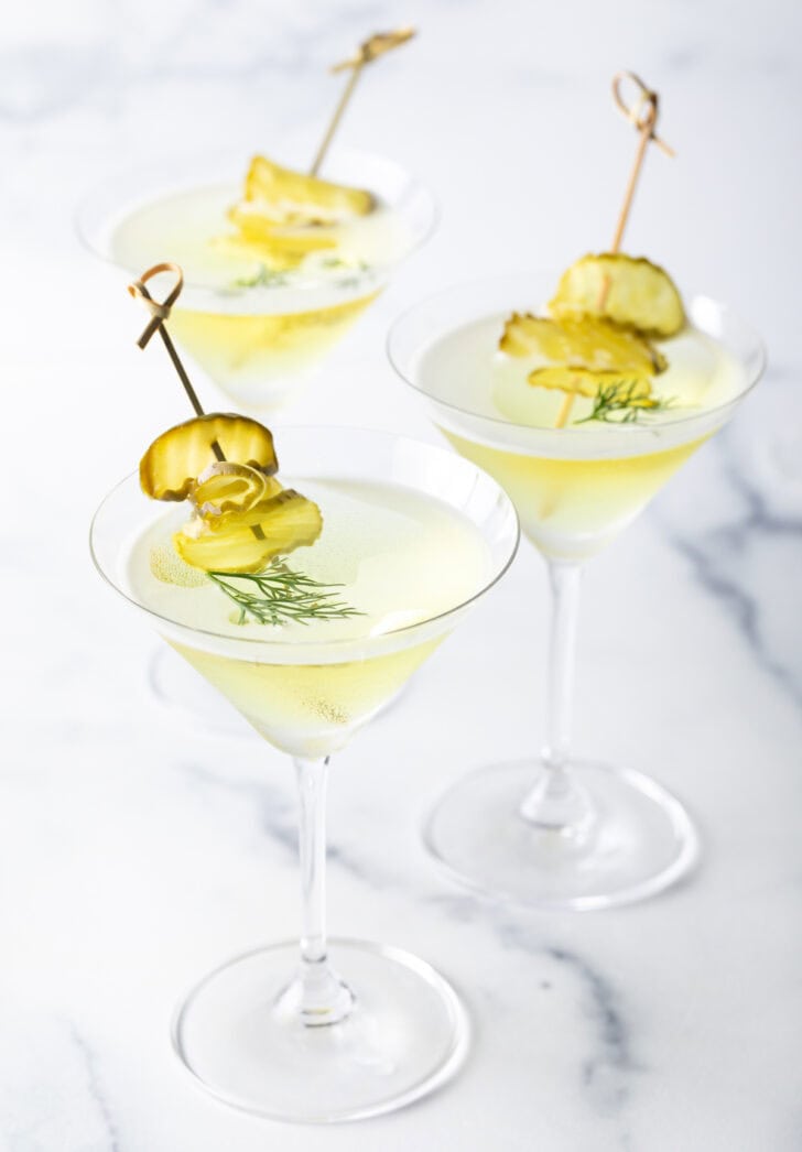 Three dirty martinis made with pickle juice and gin, garnished with skewers stacked with dill pickle slices.