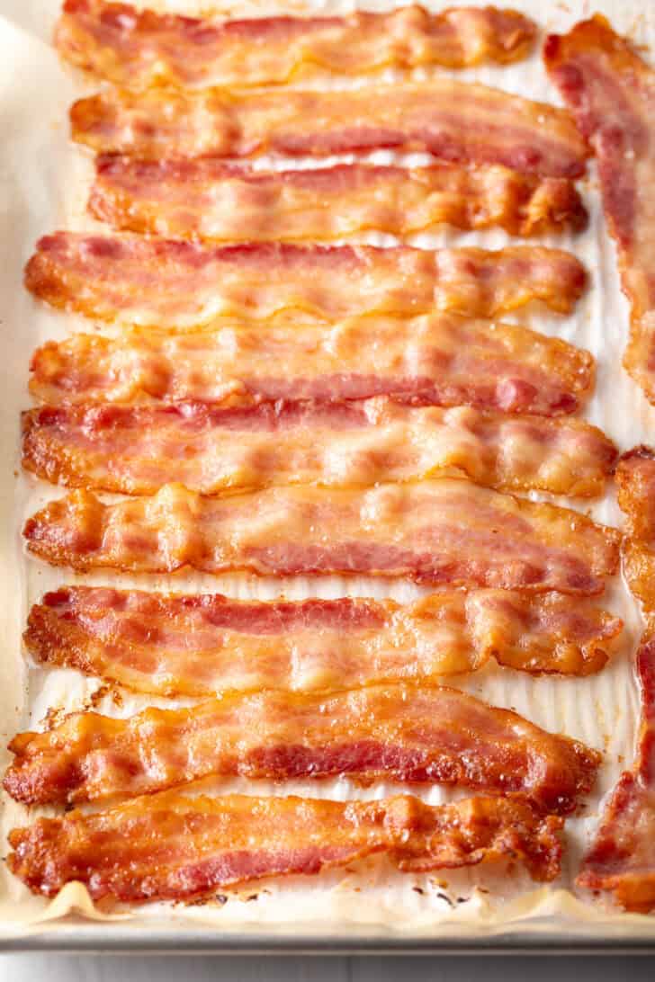 A dozen pieces of partially cooked bacon on a baking sheet.