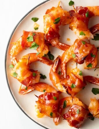 Top down white plate, nearly a dozen bacon wrapped shrimp are loaded onto the plate in a single layer.