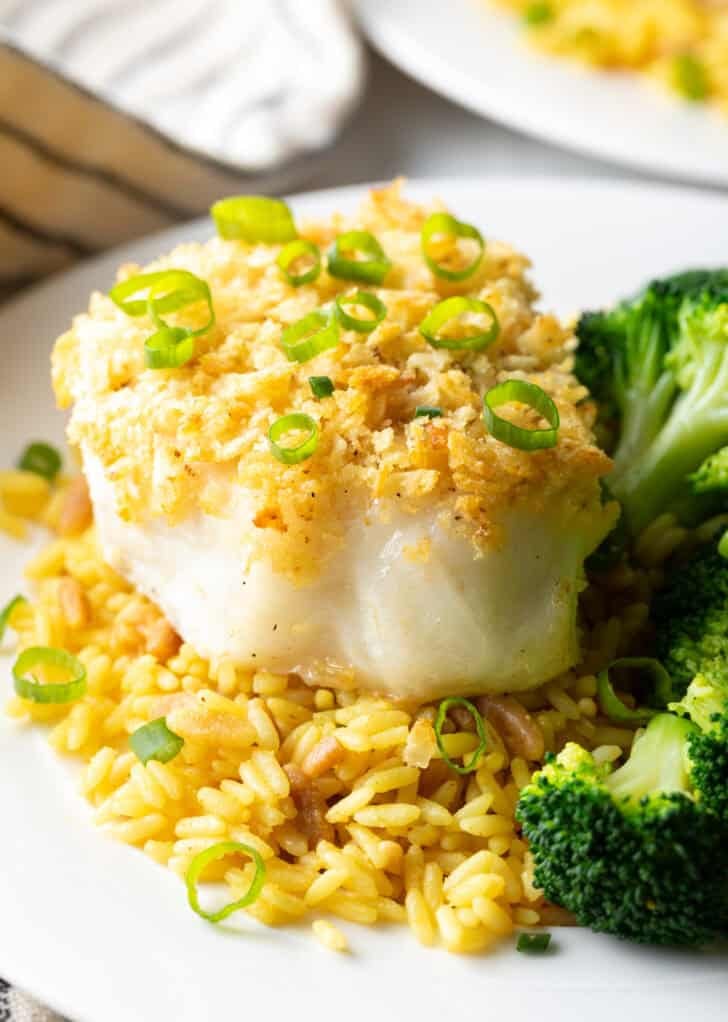 Potato chip crusted and baked bass on a plate with yellow rice and cooked broccoli.