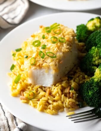 Potato chip crusted and baked bass on a plate with yellow rice and cooked broccoli.