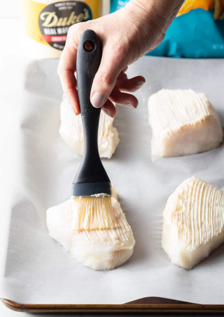 Using a black basting brush to coat 4 white grouper filets with oil and seasonings.