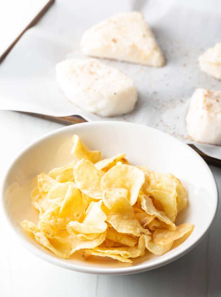 White bowl of whole chips, with 4 raw bass filets in the background.