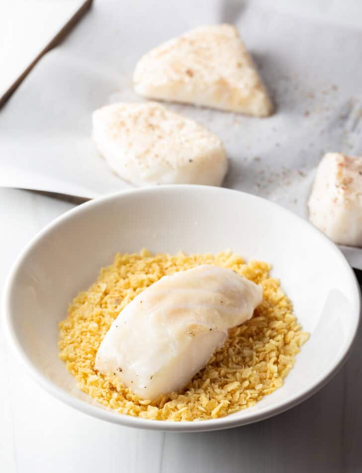 Piece of raw sea bass in a white bowl with crushed potato chips.