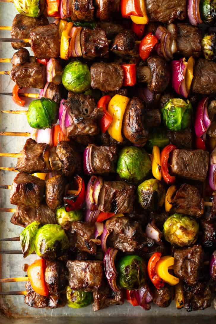 Top down view of side-by-side row of a dozen beef and veggie kabobs.