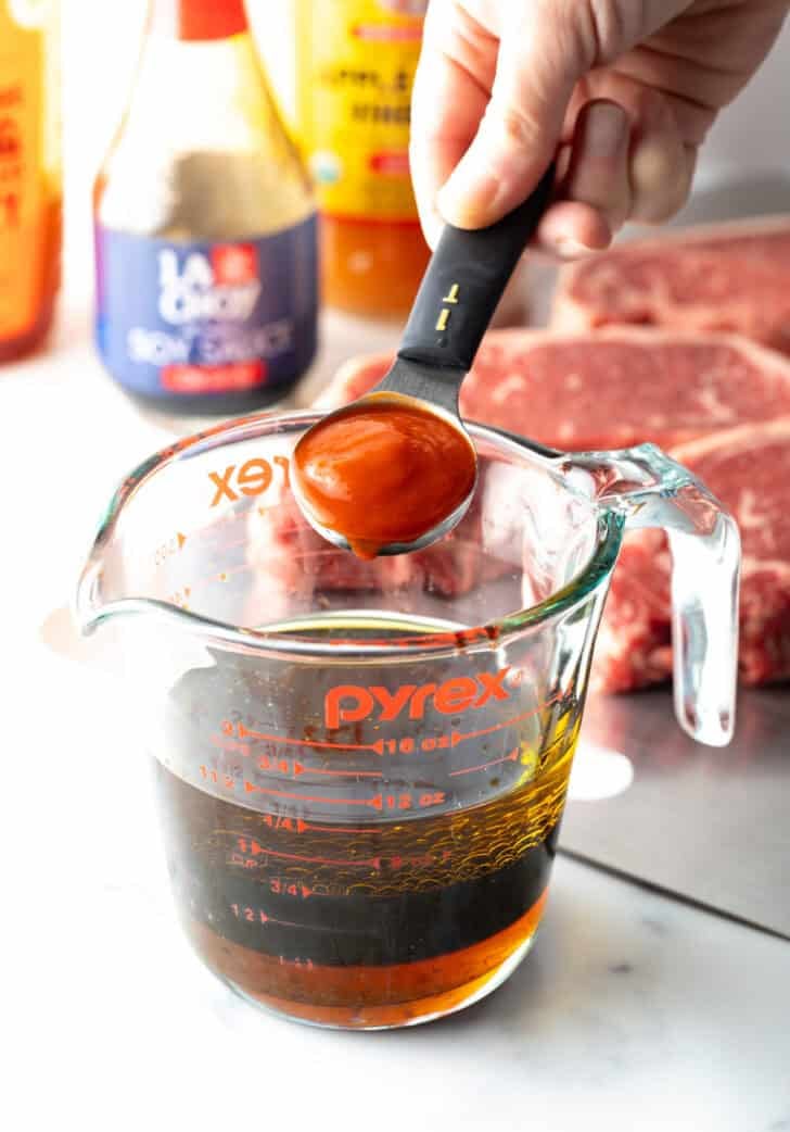 Hand adding ketchup form a tablespoon into a glass measuring cup.