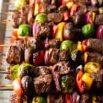 Side-by-side row of a dozen beef and veggie kabobs.