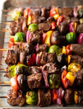Side-by-side row of a dozen beef and veggie kabobs.