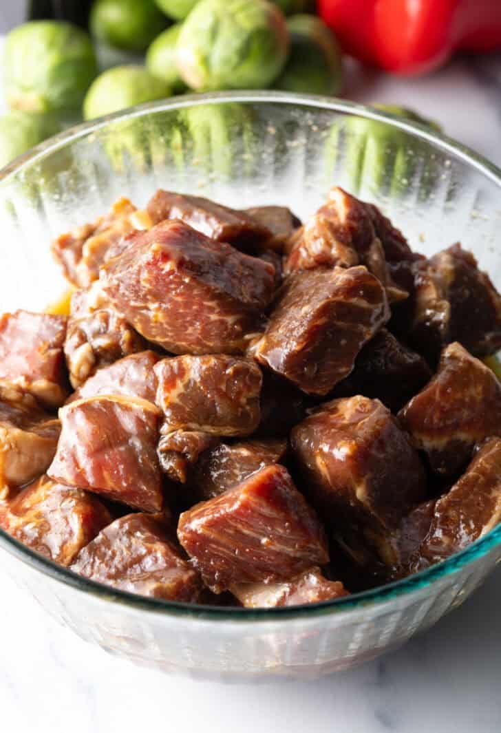 Cubes of steak marinating in a glass bowl.