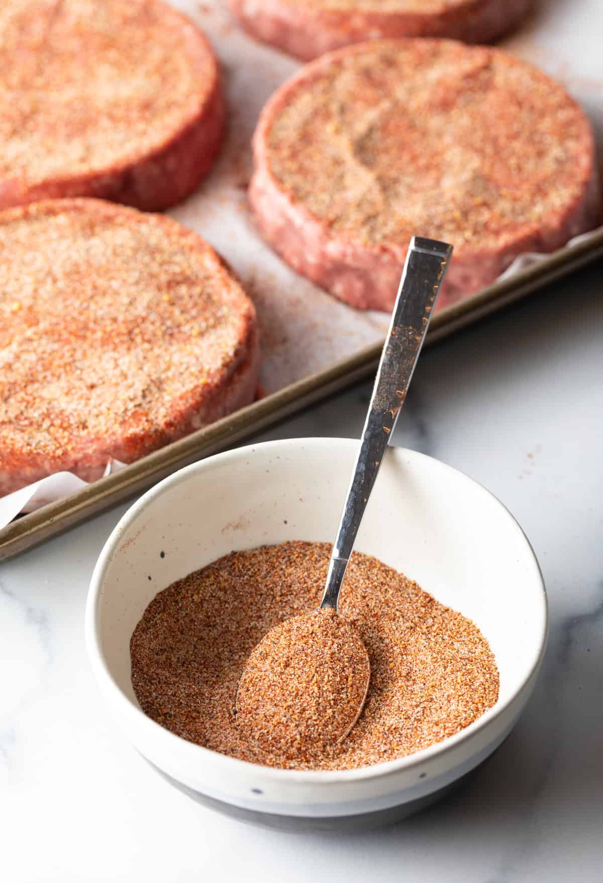 White bowl with mixture of burger seasoning and spoon.
