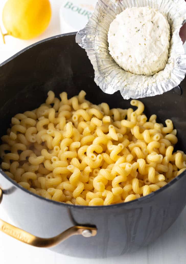 Adding cheese from a wrapper to a pot of cooked macaroni noodles.