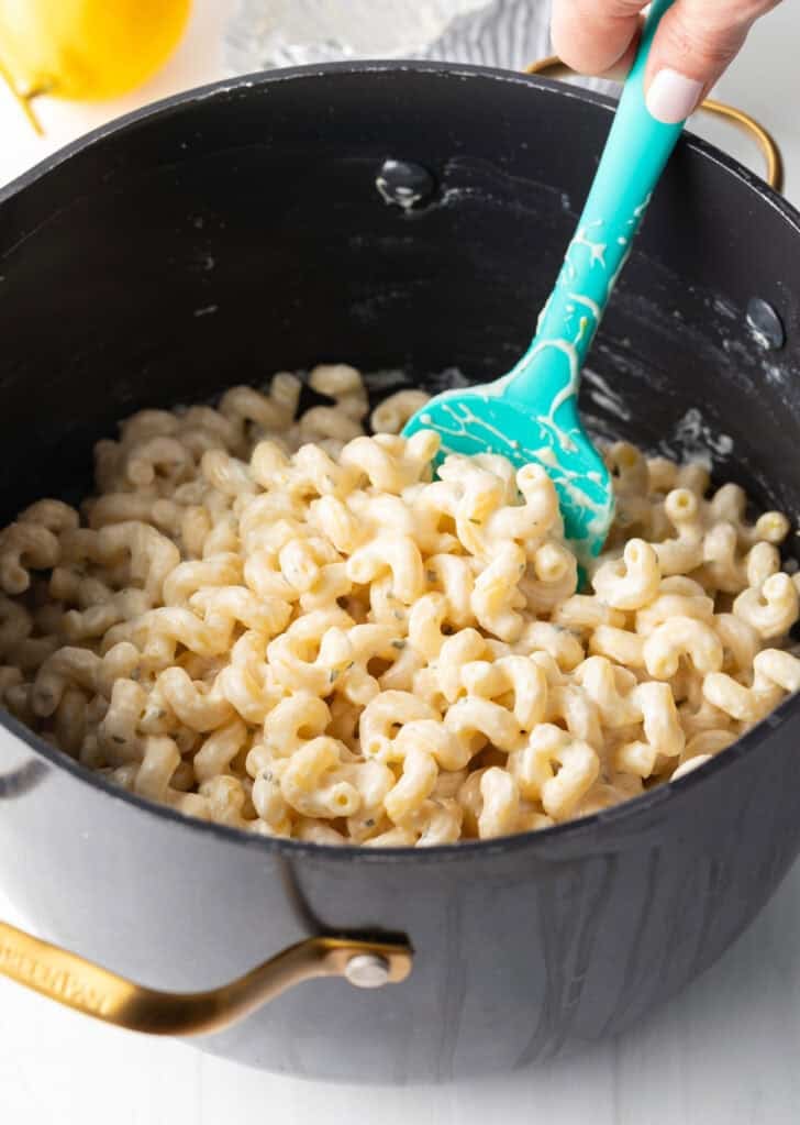 Stirring pasta and cheese sauce in a large pot with blue spatula.