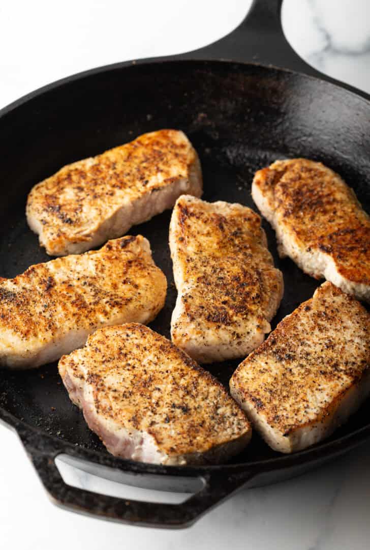6 boneless pork chops searing in a cast iron skillet.